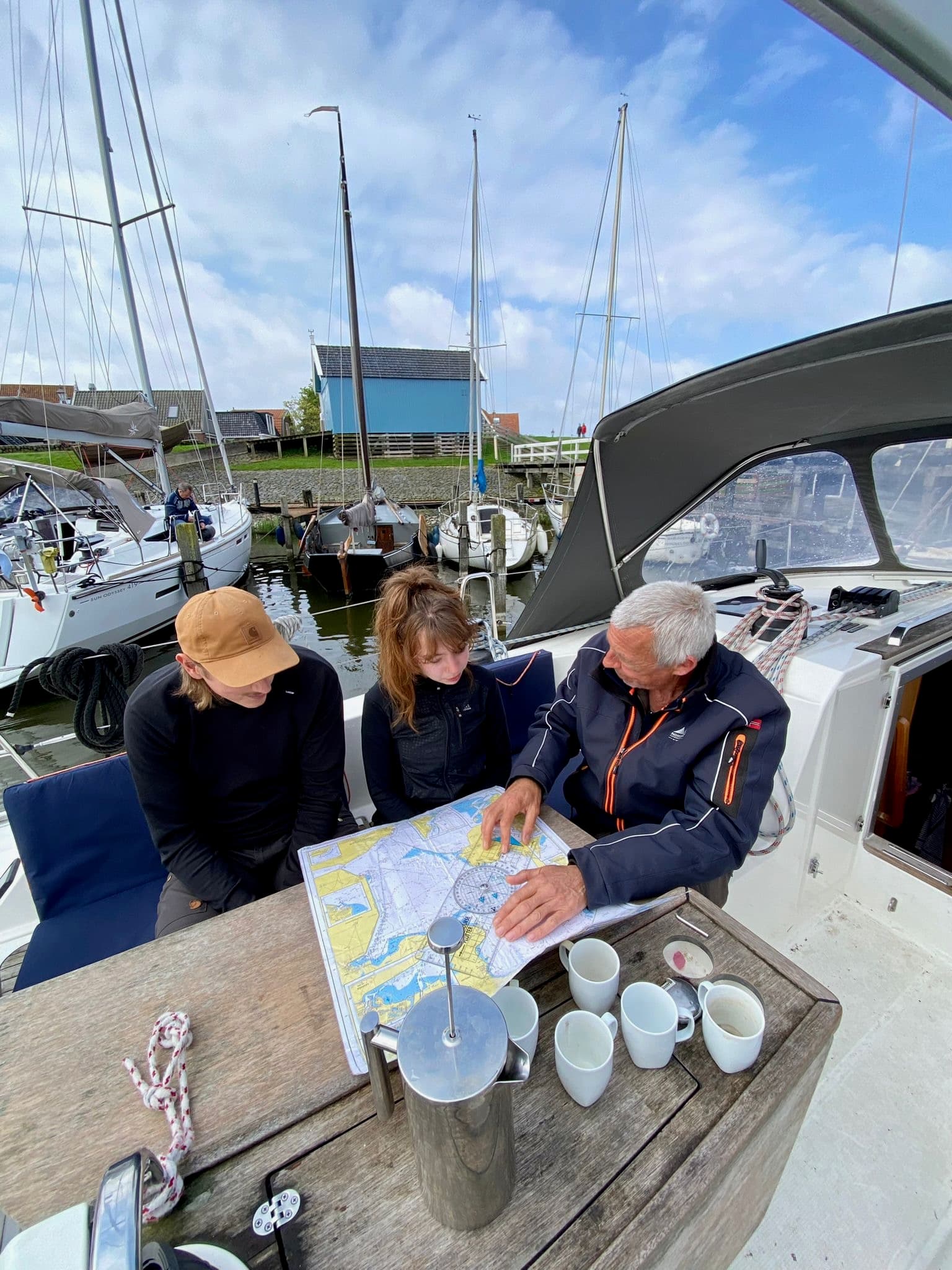 Three sailors studying a paper navigation chart in the cockpit of a moored yacht