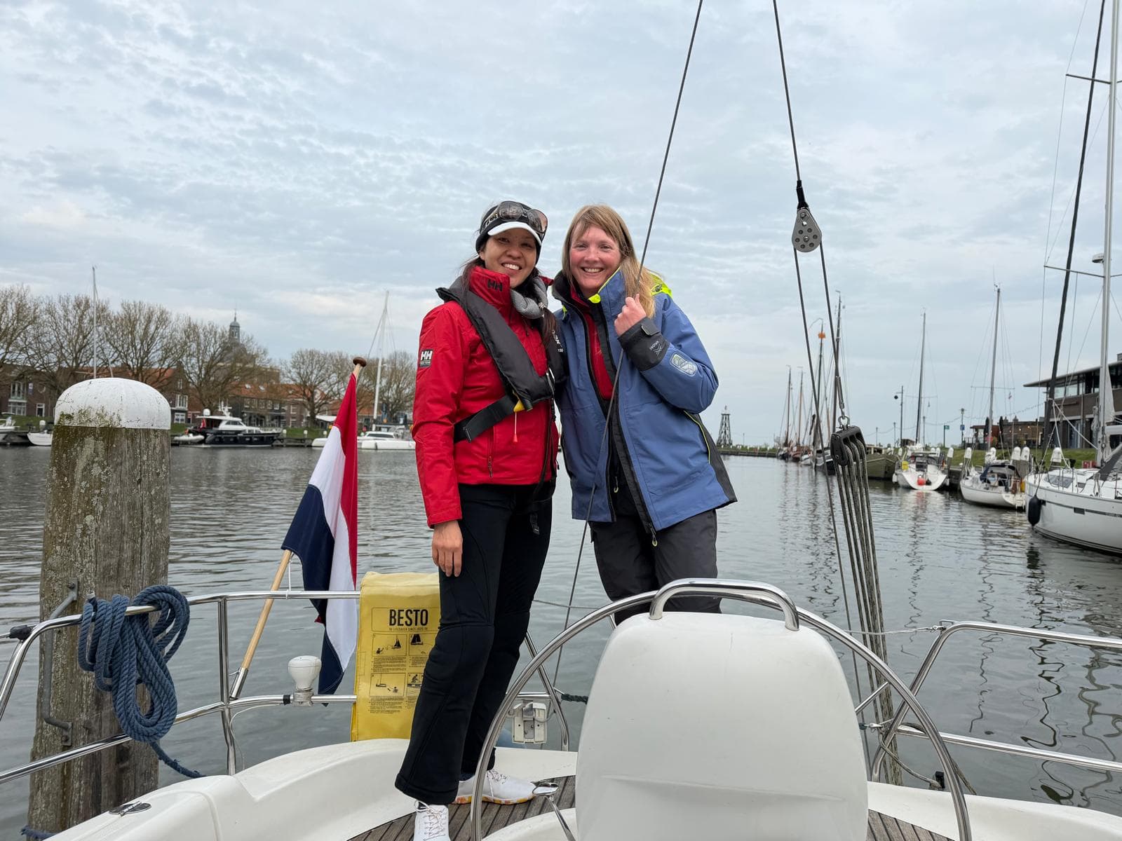 Two sailors in life vests smiling at the bow of a moored yacht in a Dutch harbour